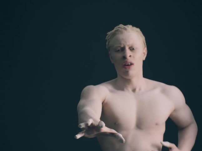 Albino black man hopping in place and reaching out with his hand to the front indoors