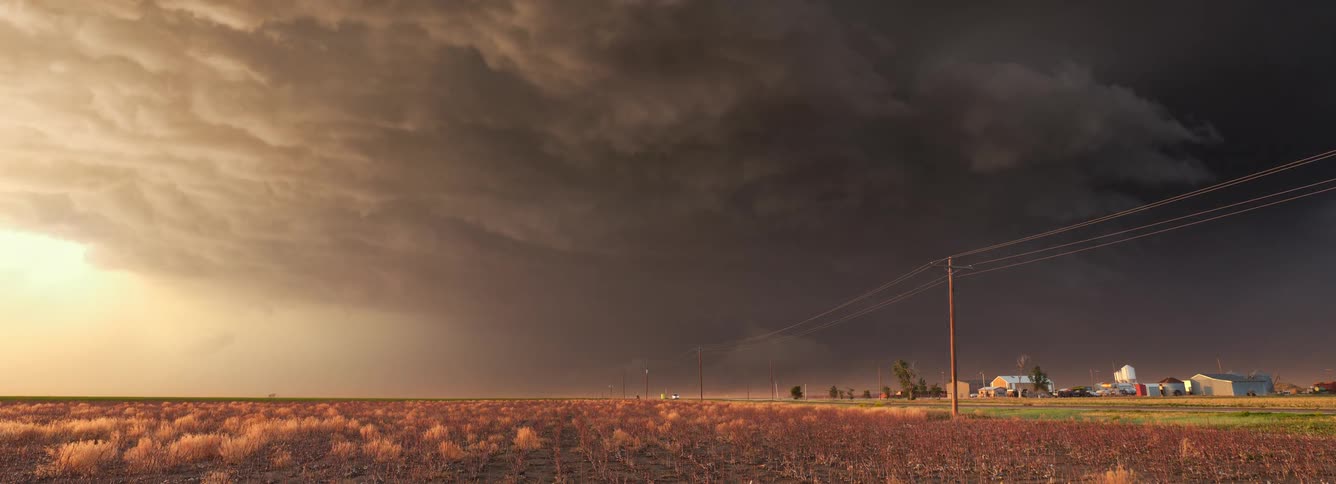 Dark storm cloud moving over a rural neighborhood with strong winds as traffic moves on the road