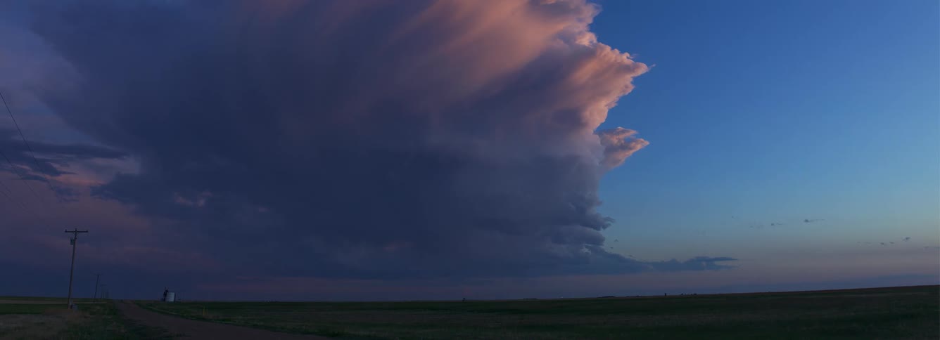 Huge cloud turns dark and lightning flashes inside as it moves across the rural landscape