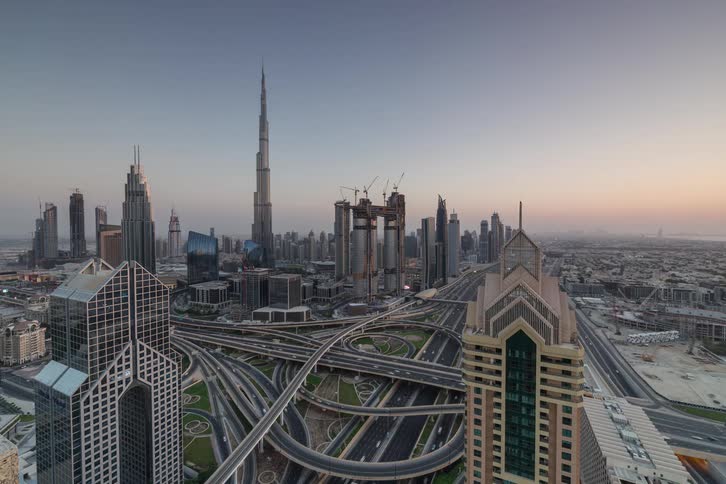 Towers and skyscrapers on the dubai city skyline as traffic moves on the busy highway interchange and lights glow when darkness falls