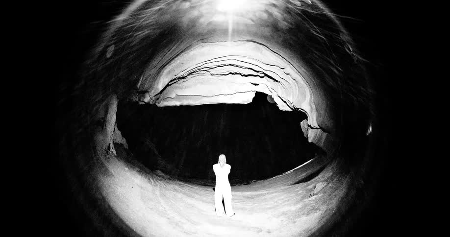 Person standing inside a large cave with an illuminated opening at the top