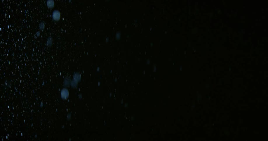 The video shows tiny particles of dust or water droplets floating and shimmering against a dark moody background a soft light catches the particles as they drift creating a subtle cinematic atmosphere of motion and texture