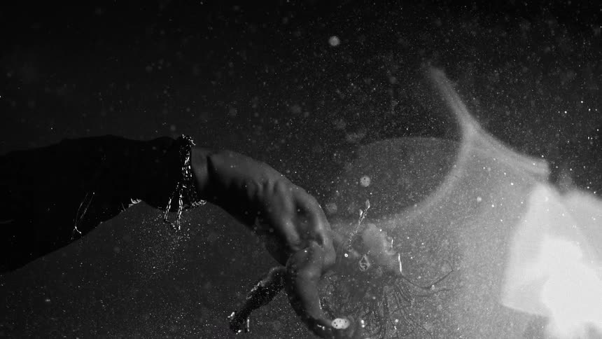 Person leaning backward under heavy rain with water splashing around and side lighting