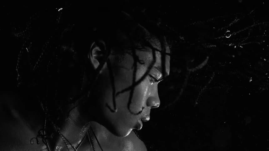 Person in profile with wet hair under rain against a dark background
