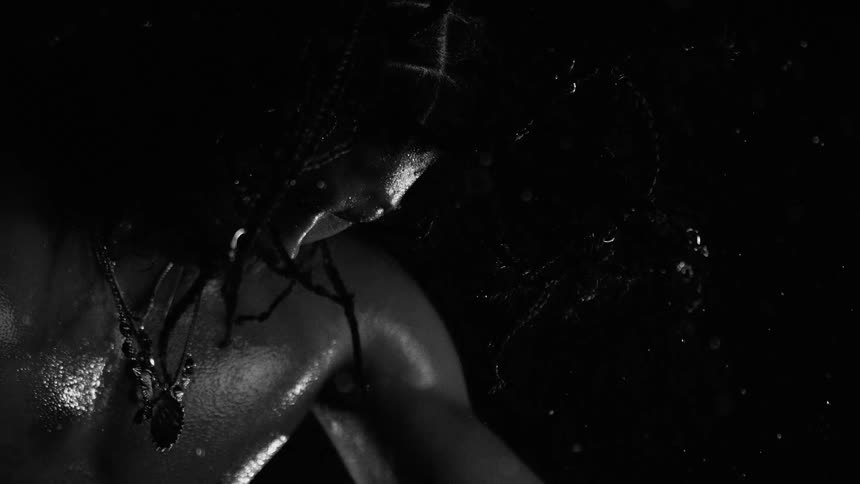Man with multiple hair braids stands outdoors at night while it rains