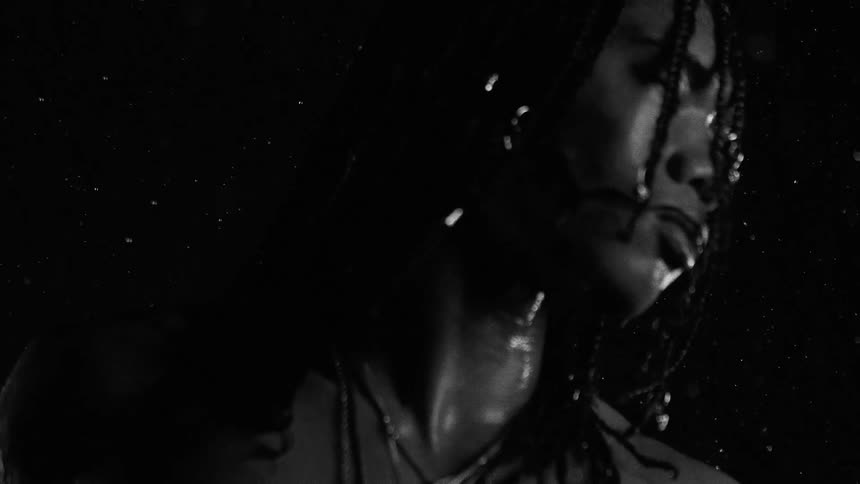 Partially illuminated face with braids under rain against a dark background