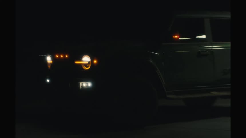 A rugged suv with its headlights on drives away from a dimly lit gas station at night