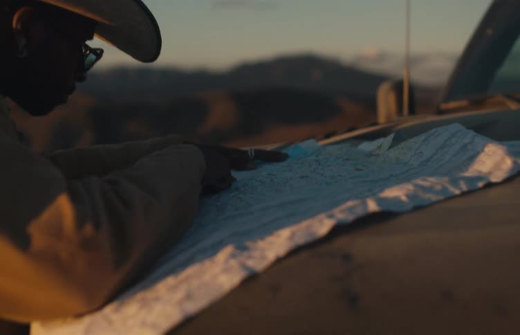A man stands with a large map spread open on the hood of his vehicle