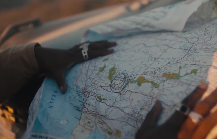 Hands wearing rings point to a circled area on an open paper map laid on a flat surface