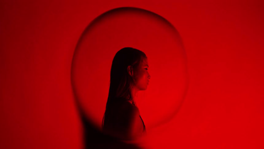 A womans profile is silhouetted against a vivid red background with a larger shadowed outline of her head projected behind her