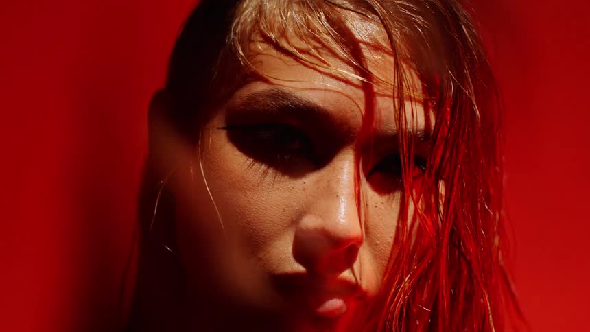 Female face with wet hair illuminated by intense red light against a dark background