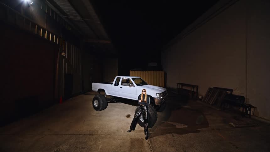 Woman sitting in front of a white pickup truck in an industrial area at night