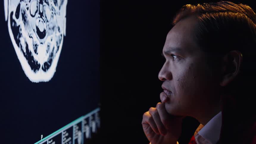 The man is examining medical imaging on the screen