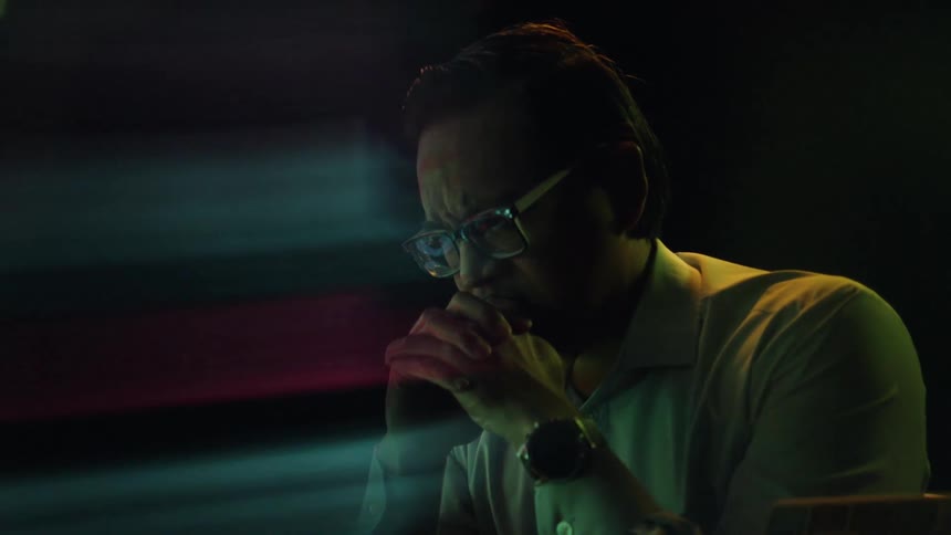 Man wearing glasses looks at screen with data reflected in the lenses in a dark environment
