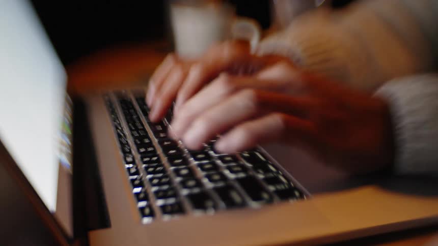 Hands typing quickly on a laptop keyboard under warm lighting