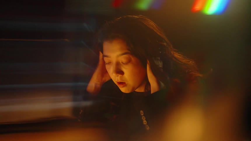 Woman with hands on her head under warm light and colorful reflections