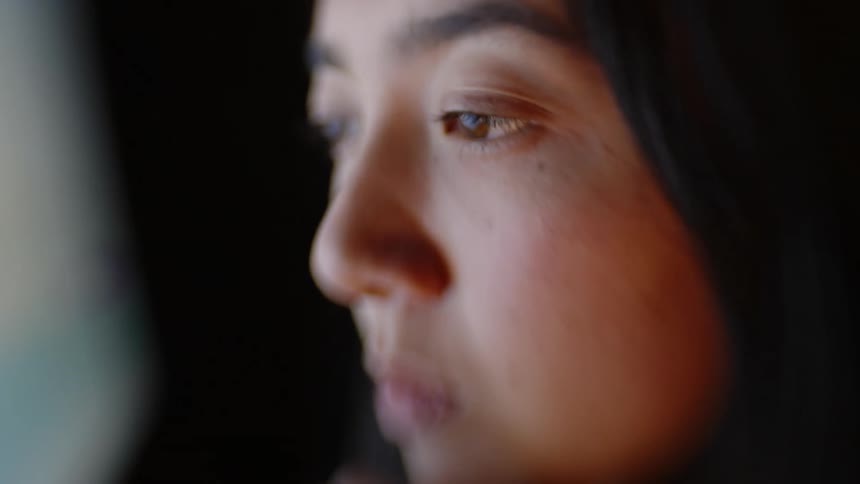 Young adult woman looking at a screen with a contemplative facial expression indoors