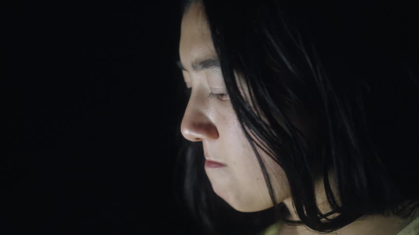 In a dimly lit setting a woman with dark hair takes a slow thoughtful sip from a blue mug the scene captures a quiet somber moment of reflection as she looks downward after drinking