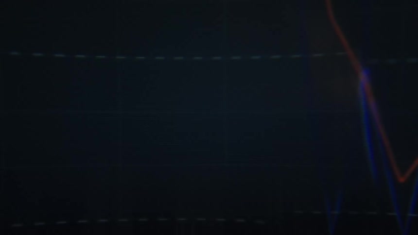 A dark screen displays fluctuating blue and red line graphs trending downward and upward against a gridlike background