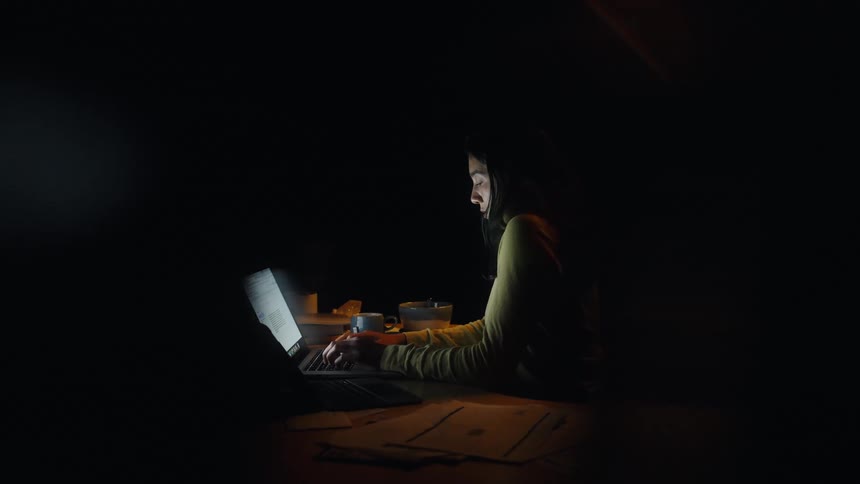 Woman works on a laptop at night with papers on the desk