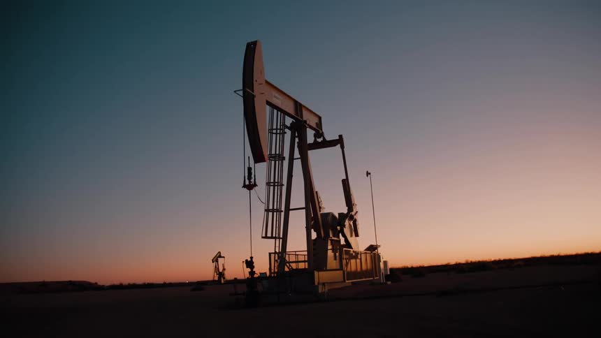 Oil pumpjack operating at dawn in an open field