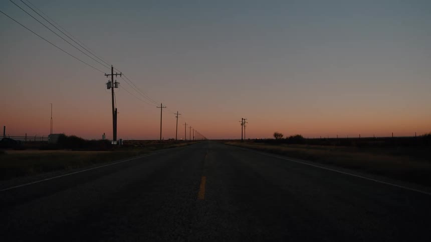 A view of a landscape with the sun setting in the distance over some fields