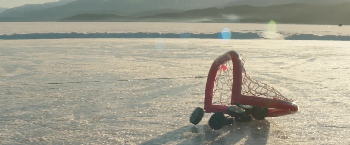 A hockey net and pucks sit on a frozen surface with a distant landscape