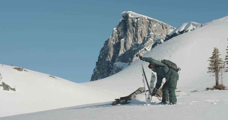 Man with a backpack secures a ski in the snow in a mountainous icy landscape