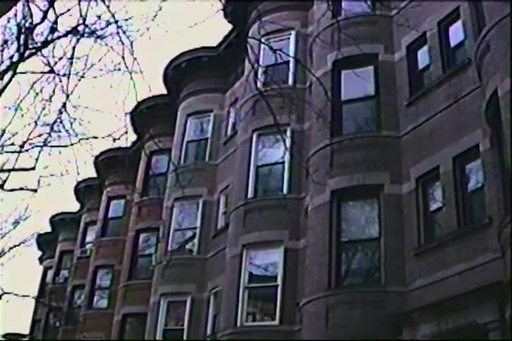A residential building with a series of glass windows and a tall leafless tree on the side at midday