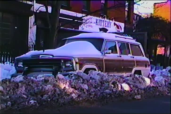 A car parked on the side of the street covered in snow during winter at sunset