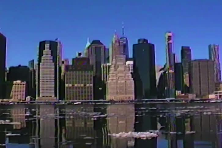 Tall skyscrapers stand along a river with chunks of white ice floating in the water under a clear blue sky