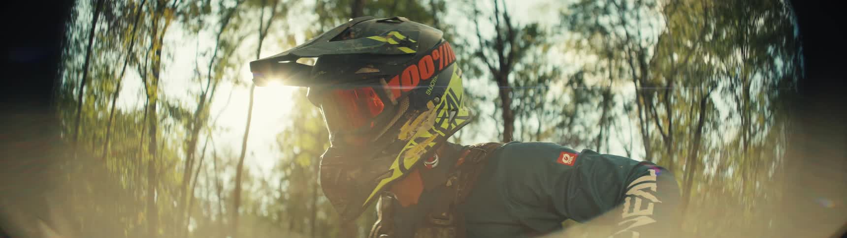 A person wearing a motocross helmet and goggles is illuminated by sunlight