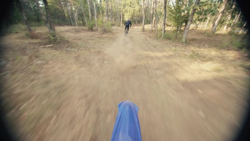 Motorcyclists speed along a dirt path through the woods on an autumn day