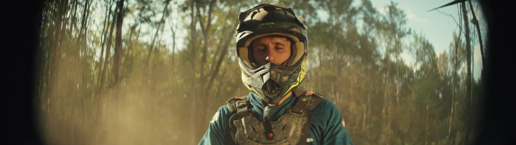 A mountain biker wearing a blue jacket and a helmet rides his bike in the woods at midday