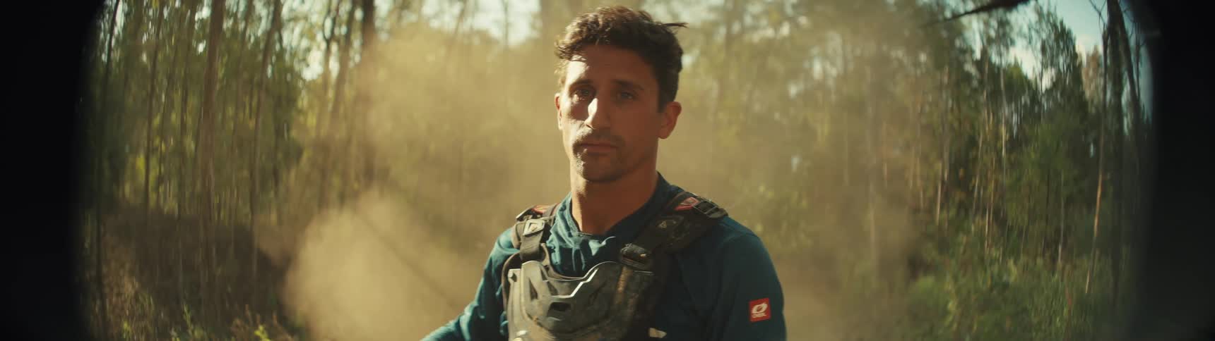 Motorcyclist sits on his dirt bike in the woods as dust floats through the air behind him