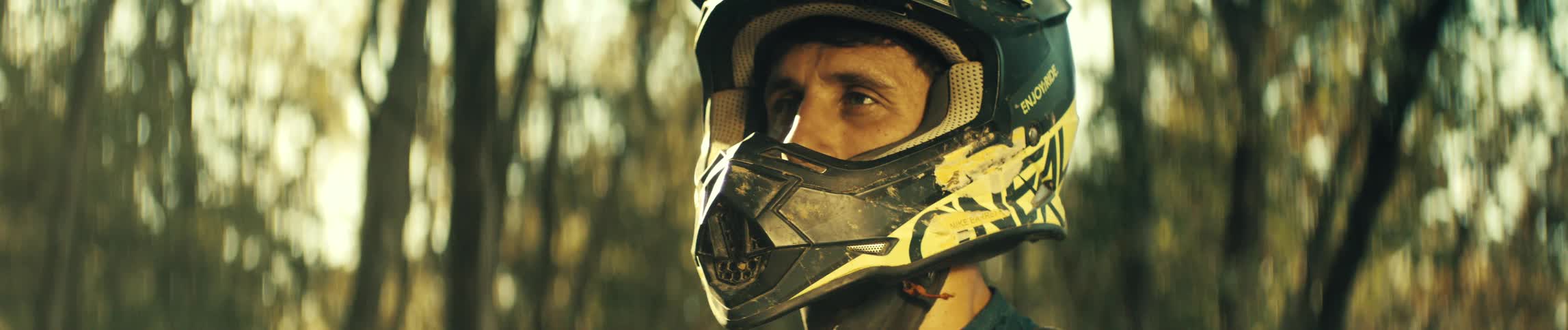A mountain biker in the woods wearing a yellow and black helmet at midday
