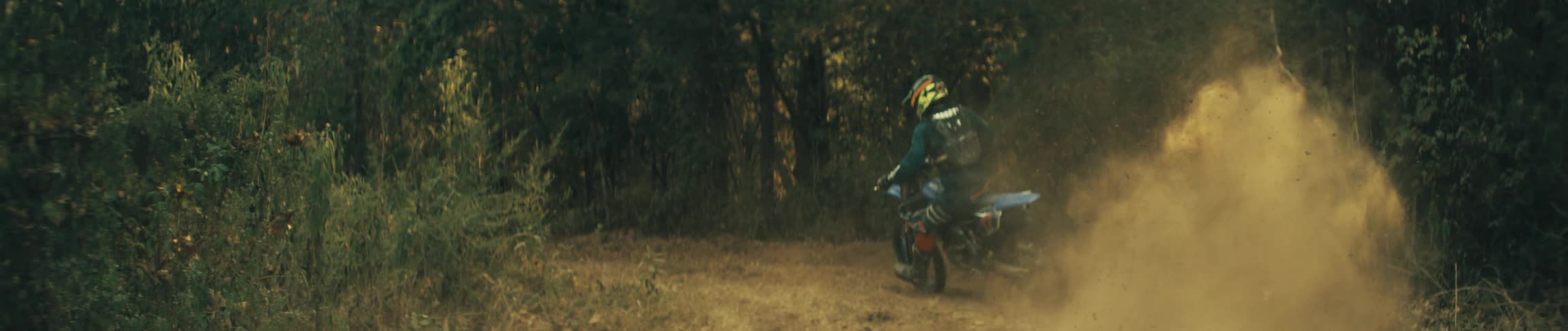 Man rides a motorbike on a trail in the woods leaving behind a cloud of smoke