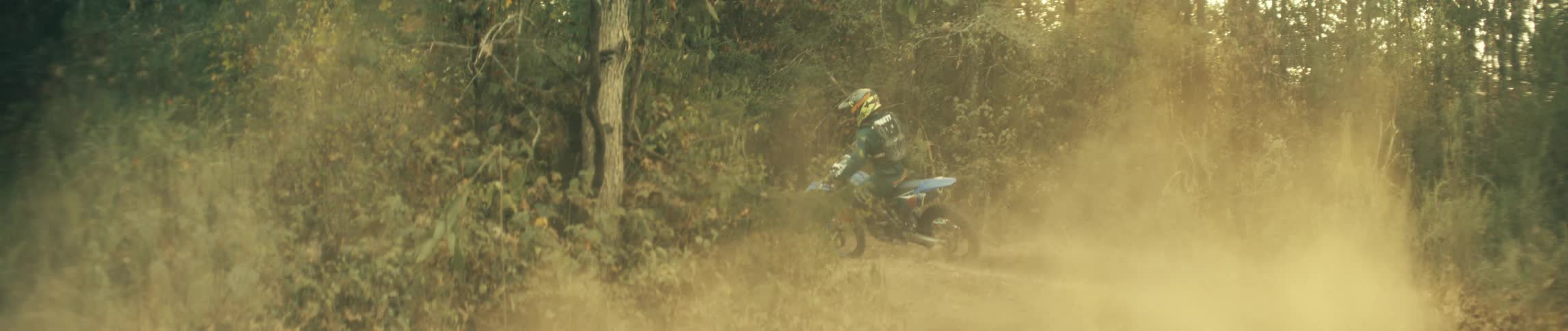 A person wearing a helmet rides a dirt bike towards a grove of trees
