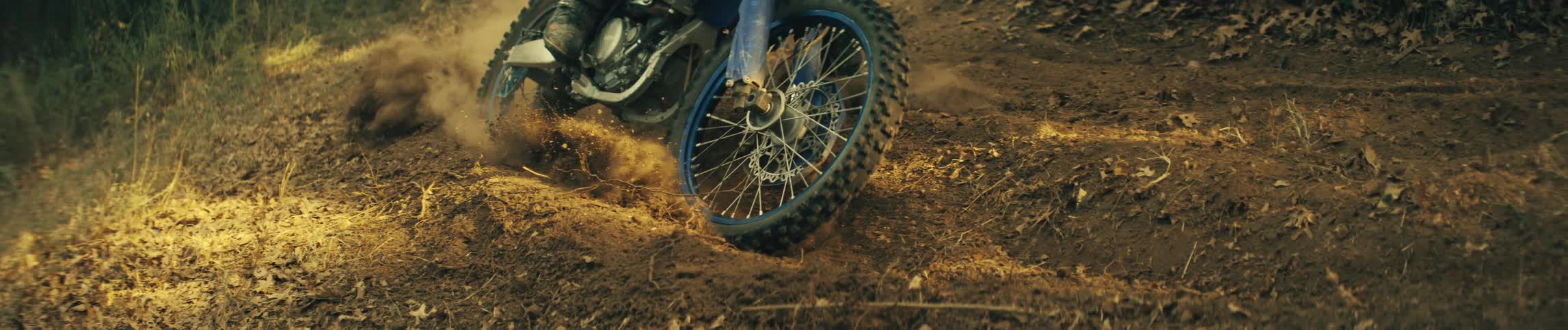 A close view of a blue motorcycle wheel turning and pressing into the soft brown soil of a dirt path during a sunny day