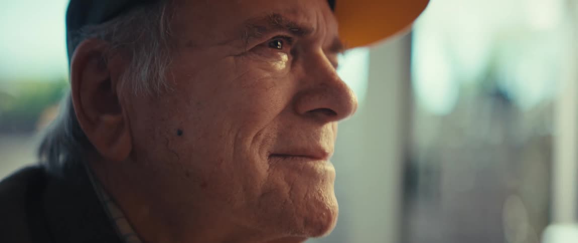 An elderly man smiles as he sits outside
