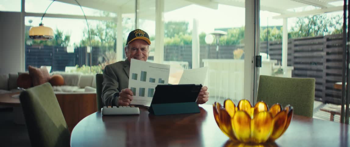 Man sitting at a table with a tablet computer looking at paperwork smiling and laughing