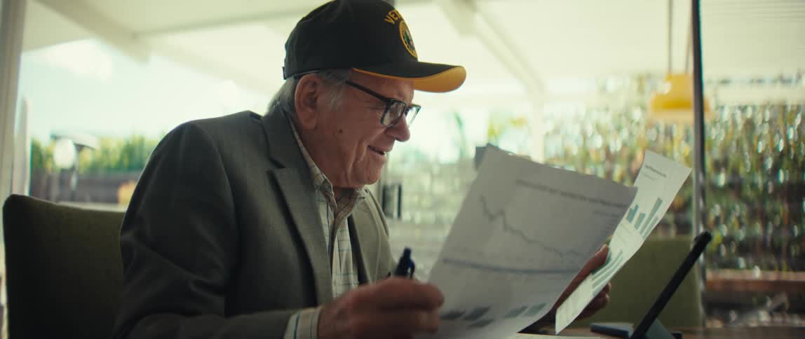 An elderly man smiles while he reviews two documents with graphs on them