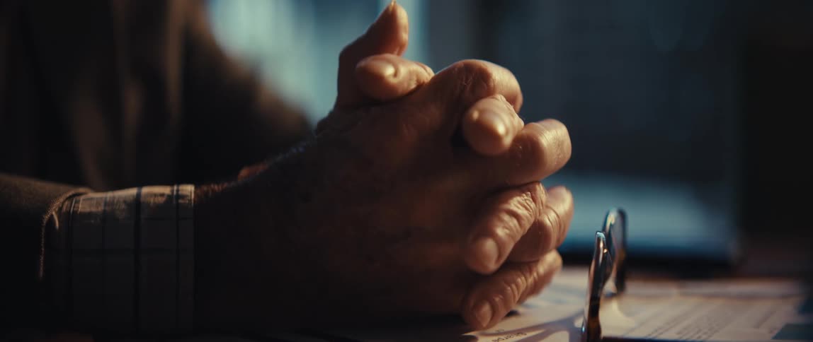 Hands of an elderly man clasping nervously against each other over sheets of paper with graphs on it indoors