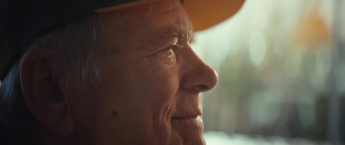 A side profile of an elderly man wearing a baseball cap as he gazes off into the distance with a gentle smile