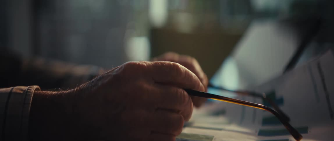 Hand holds eyeglasses over printed reports with charts next to a tablet