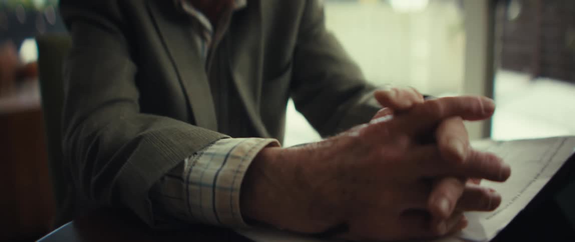 Hands clasped over documents next to a tablet resting on the table