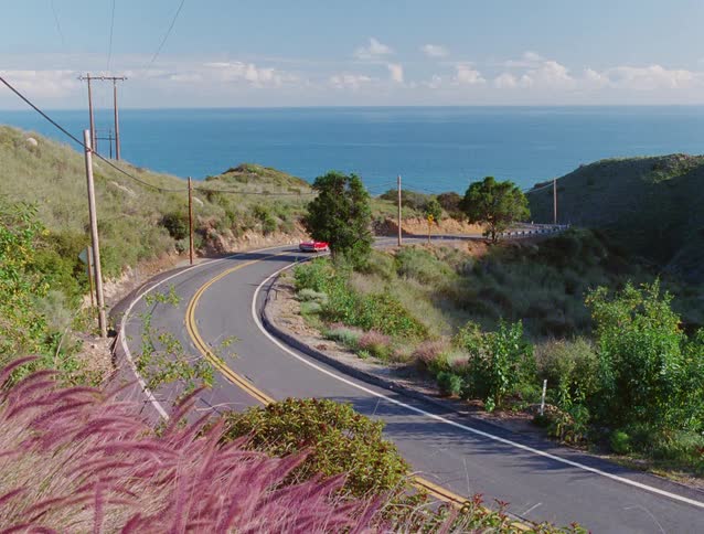 Red convertible drives along a winding coastal road with an ocean view