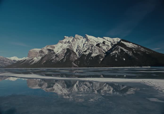A snowcovered mountain is reflected in a partially frozen body of water