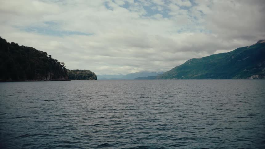 River flows between forested mountains under a cloudy sky