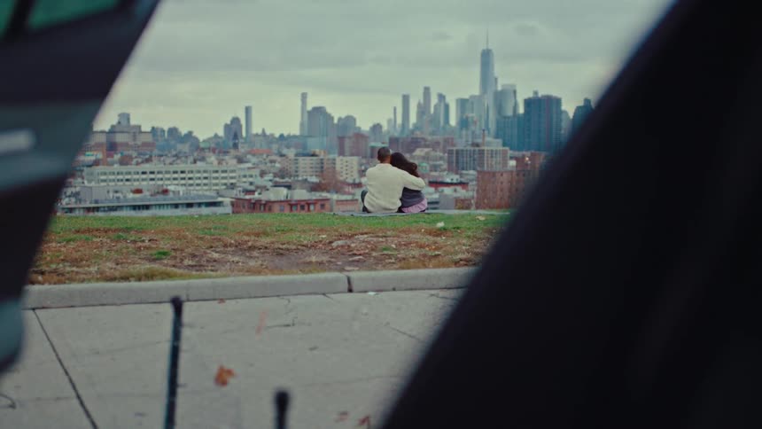 A couple sits holding each other looking at the skyline as a man jogs past